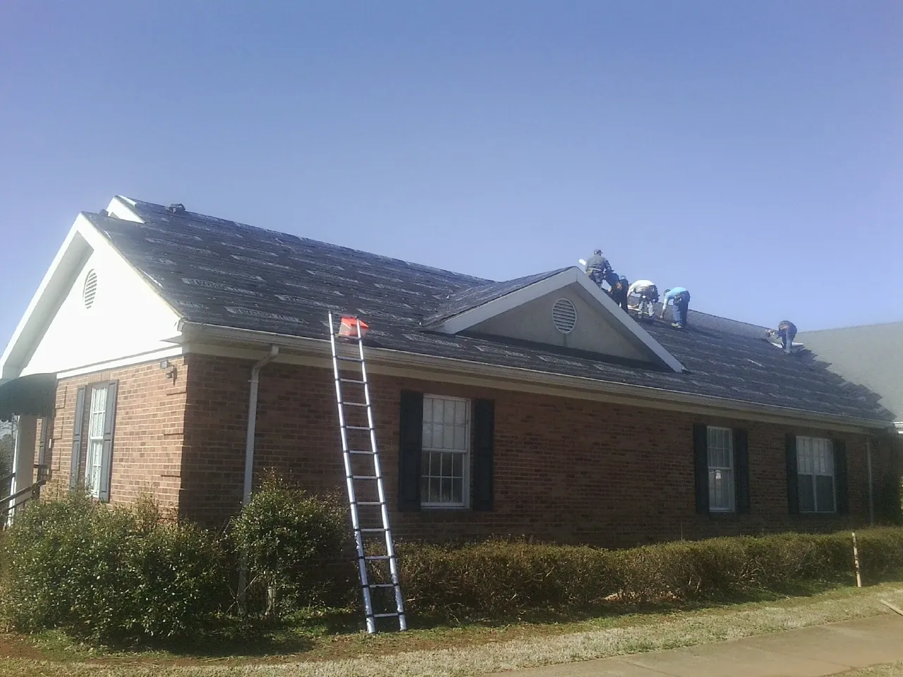 Crew tearing shingles off a brick ranch roof with a ladder set — Emergency Roof Repair work by our crew in Wattsburg
