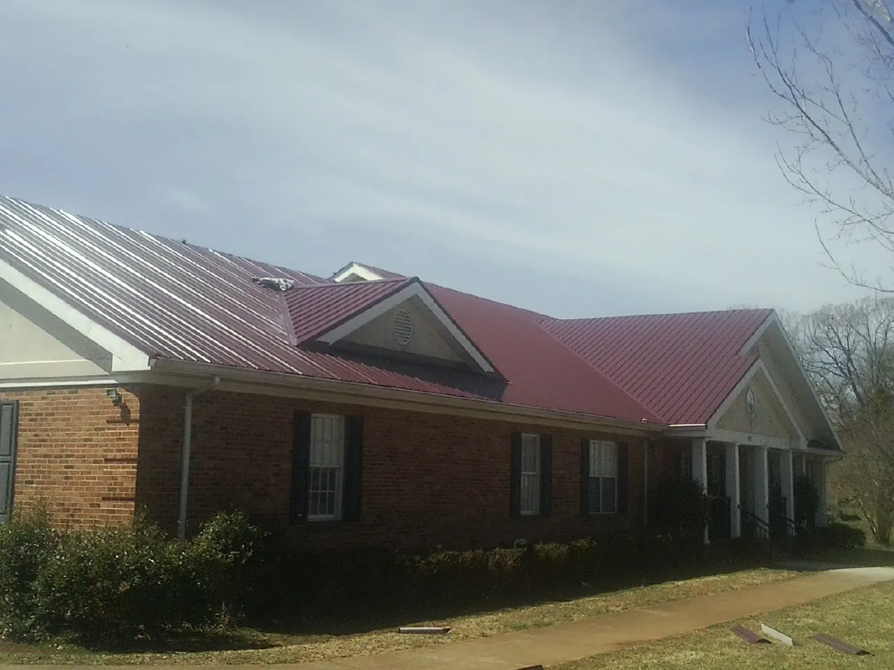 Red metal roof with gabled entries on a long brick building, from a Hail Damage Roof Repair job in Wattsburg