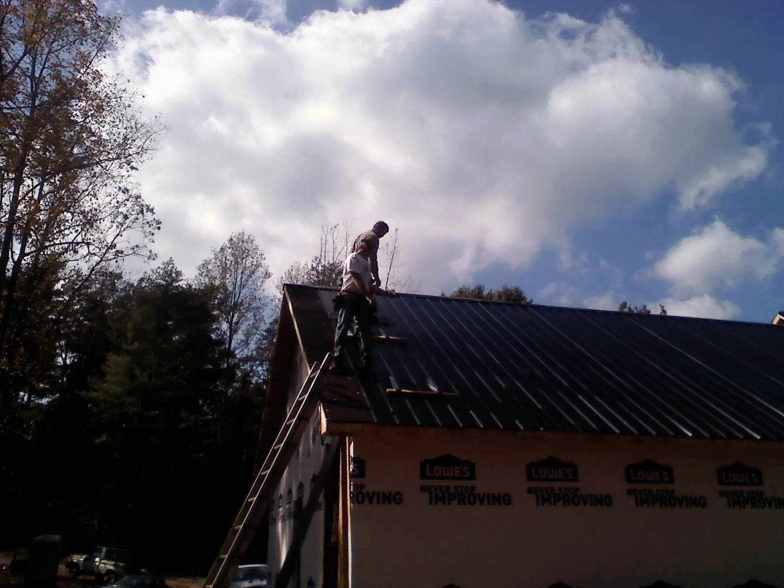 Roofer fastening dark metal panels high against a cloudy sky, from a Roof Inspection job in Wattsburg