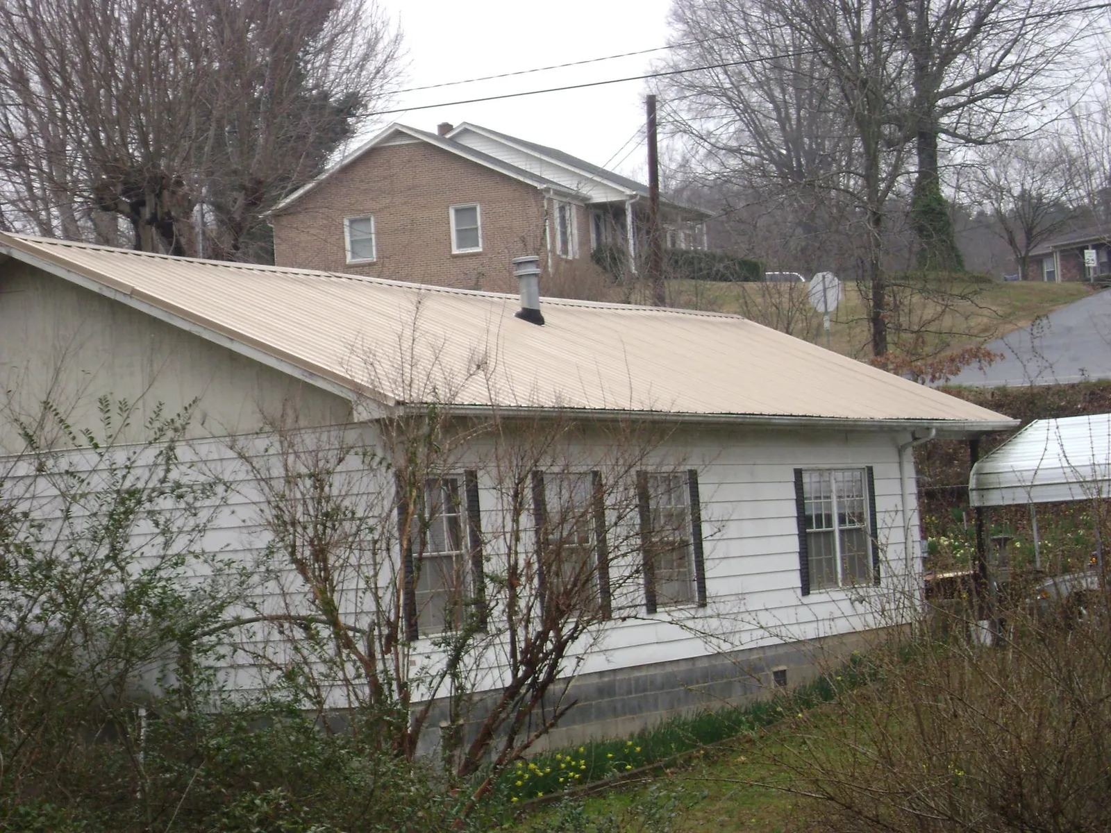 Tan metal roof on a white sided house set into a hillside — Commercial Roofing by Roofing Brothers in Wattsburg