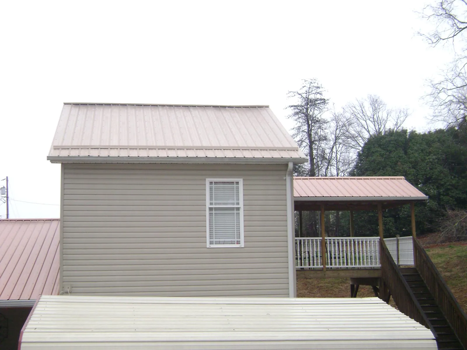 Tan metal roofs on a two story addition and attached porch, from a Roof Replacement job in Wattsburg