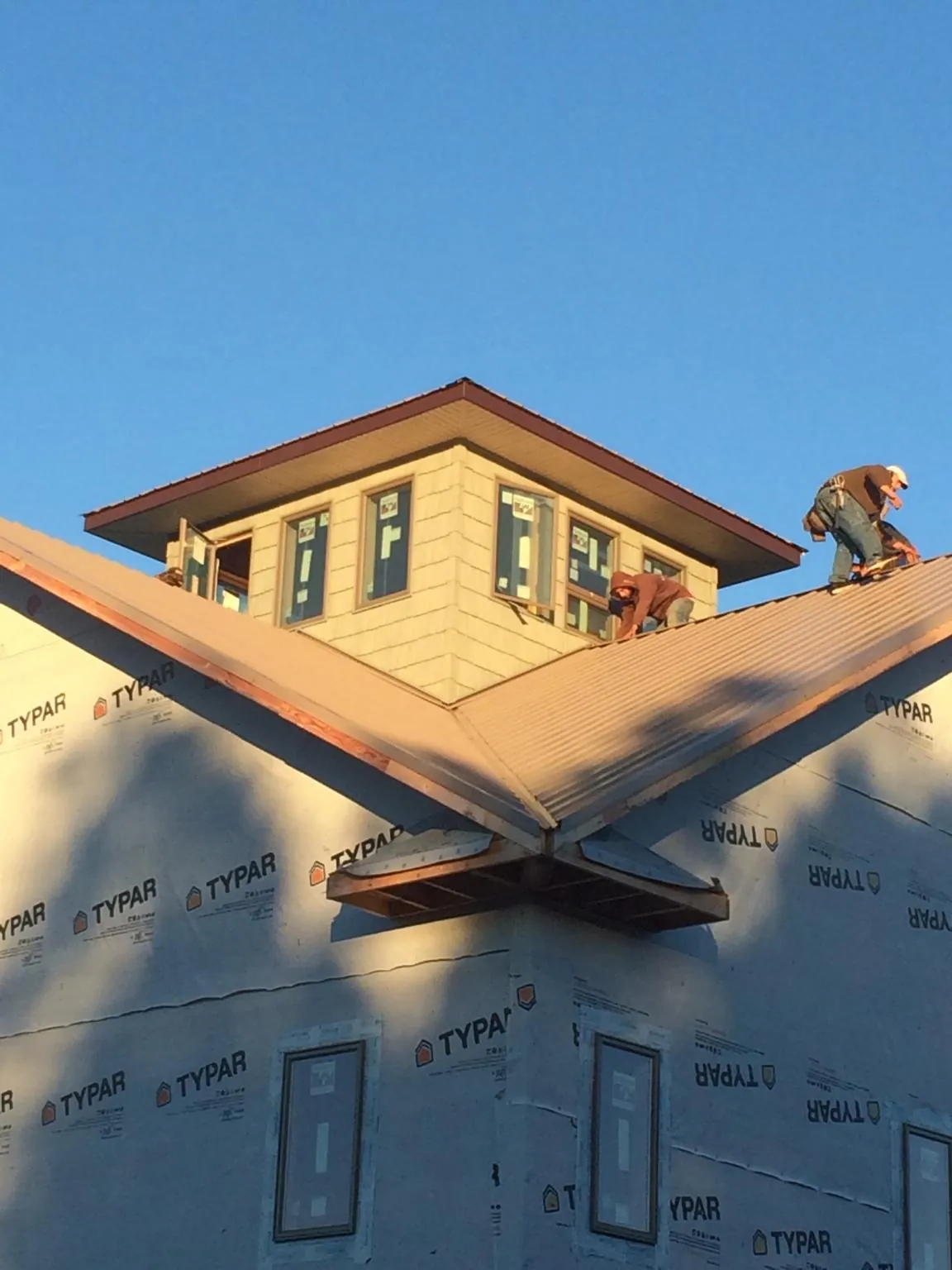 Roofers working around a rooftop cupola on a new metal roof at sunset in Wattsburg
